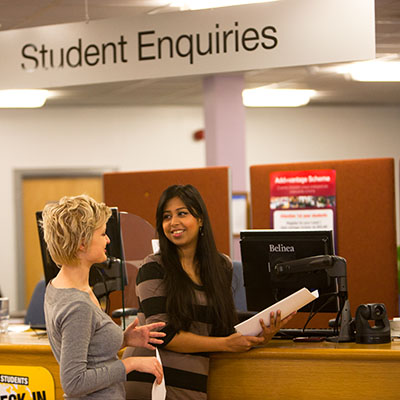 two-female-students-standing-at-student-enquiries-desk