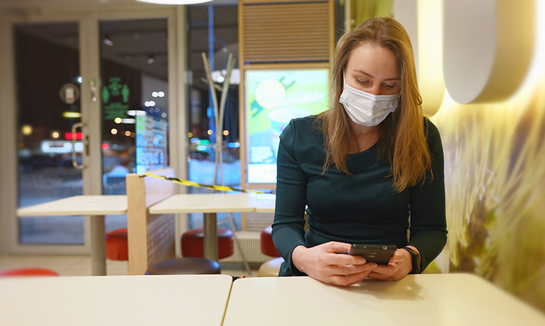 A lady in a restaurant, wearing a COVID mask, on her phone