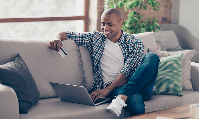 A man sat on the sofa with a laptop and a credit card in his hand