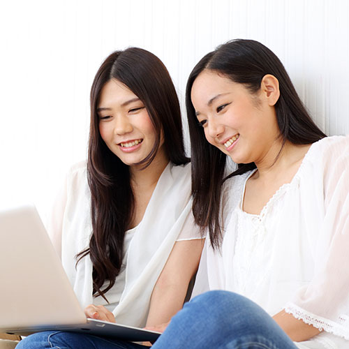 2-female-asian-students-sitting-and-looking-at-laptop